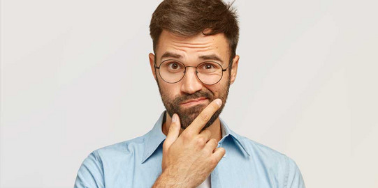 FAQs Mann mit blauem Hemd und Brille hält sich fragend die Hand an das Kinn