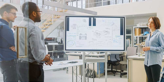 Know-How drei Personen stehen vor einer Bildschirmpräsentation