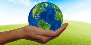 Nachhaltigkeit One hand holds a globe against the background of a green meadow with a blue sky.