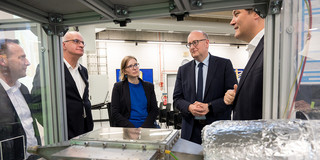 Mehrere Personen diskutieren an einem technischen Gerät hinter Glas.